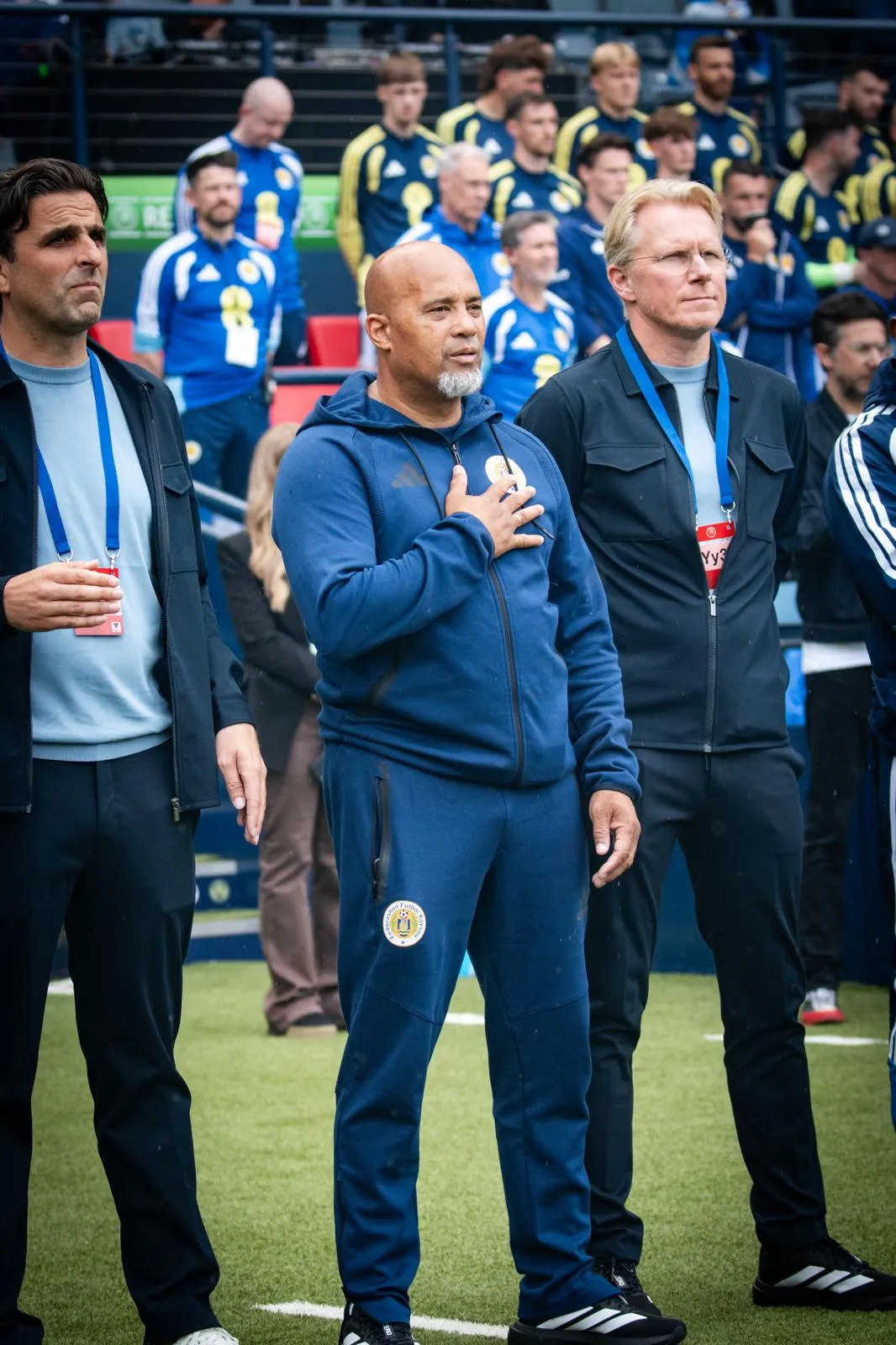 Curaçao-perschef Vincent Schildkamp (rechts) luisterend naar het volkslied, naast assistent-trainer Dean Gorré en teammanager Wouter Jansen.